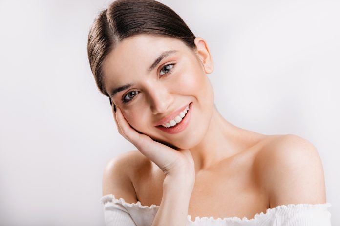 Portrait of smiling girl with healthy skin. Cute dark-haired woman looking at camera on white background.